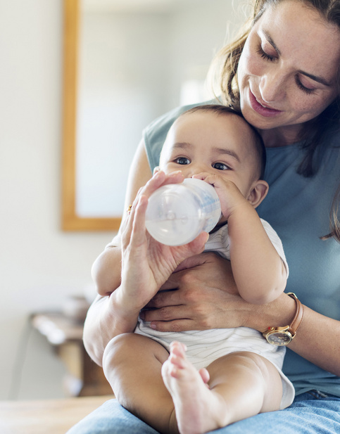 baby drinking milk from bottle on moms lap