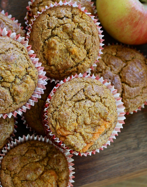 Frische Apfel-Zimt-Muffins auf einem Holzbrett, daneben rote Äpfel.